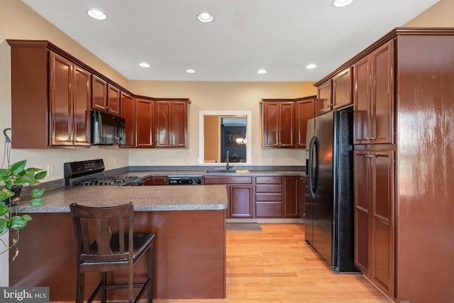 kitchen with a sink, black appliances, a peninsula, recessed lighting, and light wood-style flooring