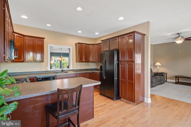kitchen with a sink, light wood-style flooring, a peninsula, open floor plan, and black appliances
