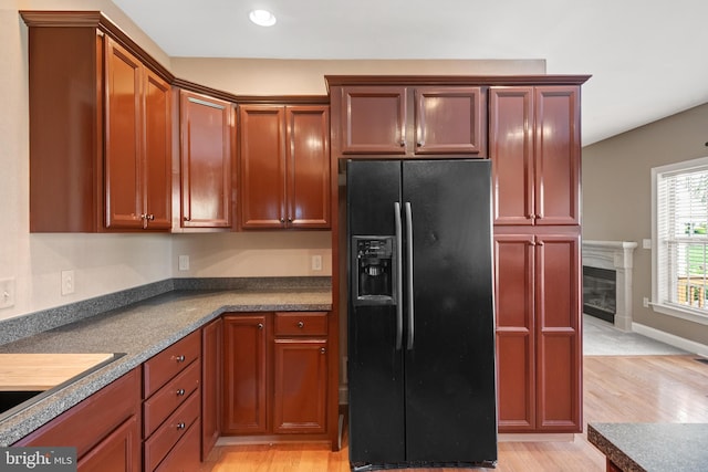 kitchen with black refrigerator with ice dispenser, dark countertops, light wood-style floors, recessed lighting, and a high end fireplace