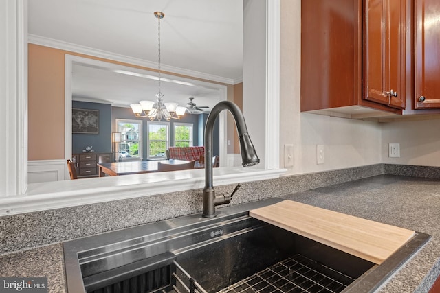 room details with crown molding, brown cabinetry, dark countertops, a chandelier, and a sink