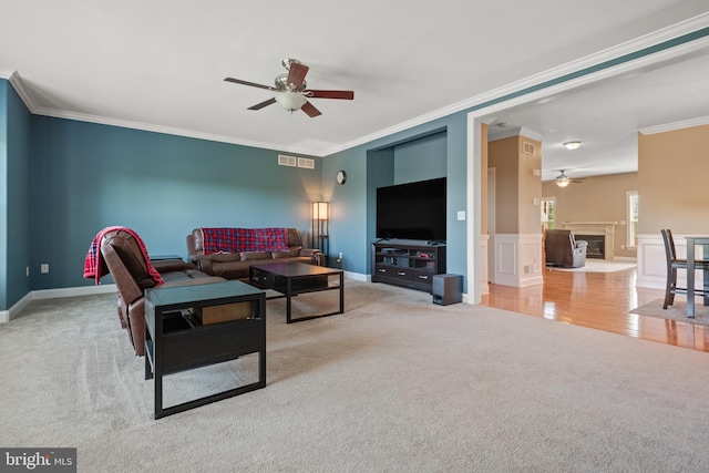living area featuring ornamental molding, a glass covered fireplace, carpet flooring, baseboards, and a ceiling fan