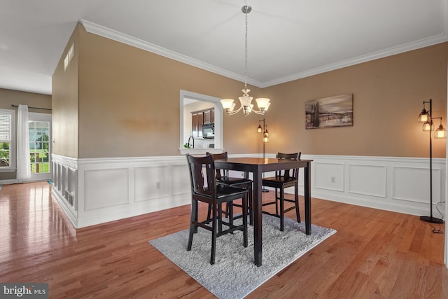 dining space featuring ornamental molding, wood finished floors, a notable chandelier, and a wainscoted wall