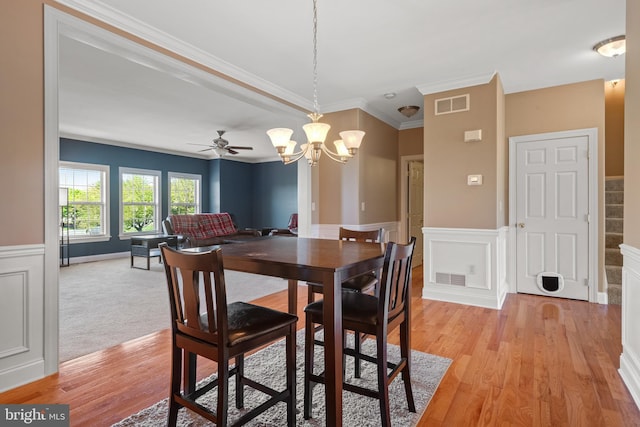 dining area featuring visible vents, ornamental molding, a wainscoted wall, and light wood-style floors
