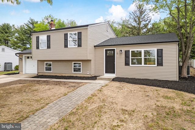 split level home with an attached garage, a chimney, central AC, and driveway