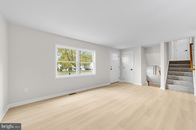 unfurnished living room featuring baseboards, stairway, light wood-style flooring, and visible vents