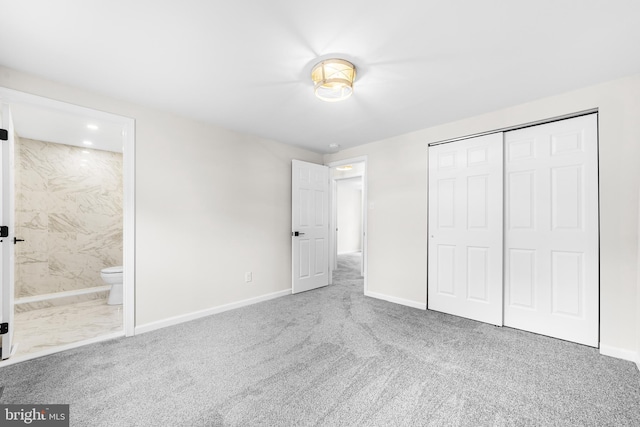 unfurnished bedroom with carpet flooring, a closet, ensuite bathroom, and baseboards