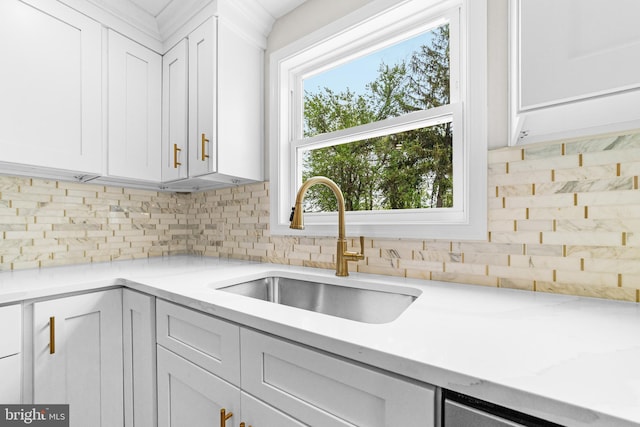 kitchen with backsplash, light stone counters, white cabinets, and a sink