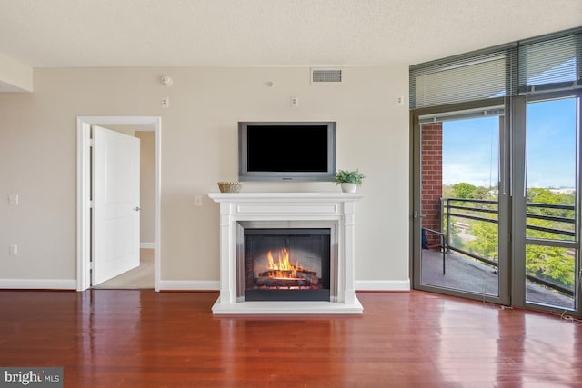 unfurnished living room featuring wood finished floors, visible vents, baseboards, and a lit fireplace