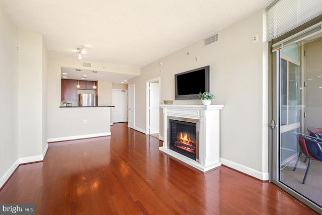unfurnished living room featuring visible vents, a glass covered fireplace, baseboards, and wood finished floors