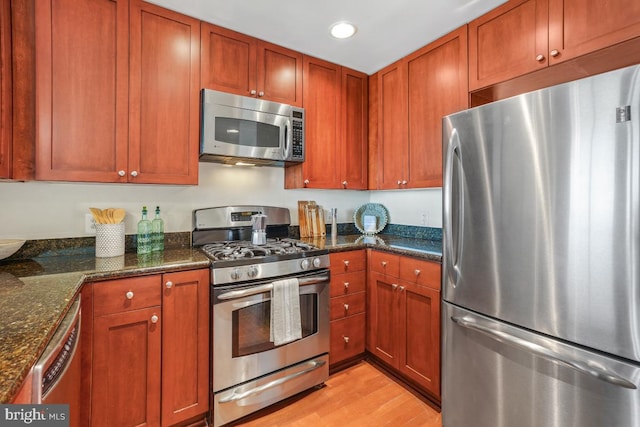 kitchen with light wood-type flooring, recessed lighting, dark stone countertops, and appliances with stainless steel finishes