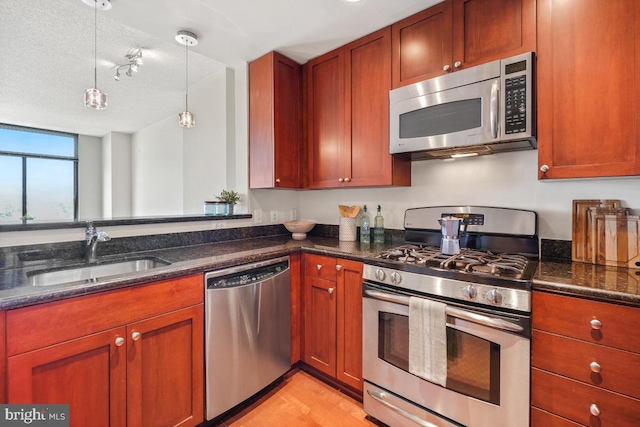 kitchen featuring a sink, stainless steel appliances, dark stone countertops, light wood-type flooring, and hanging light fixtures