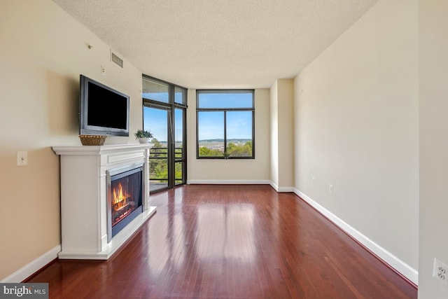 unfurnished living room with a warm lit fireplace, wood finished floors, a wall of windows, baseboards, and a textured ceiling