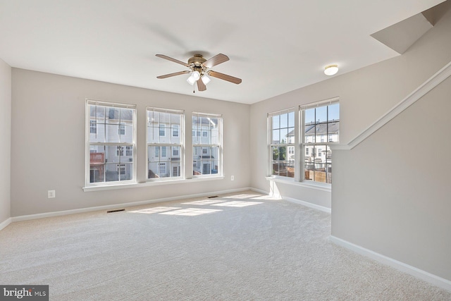 carpeted spare room with baseboards, ceiling fan, and visible vents