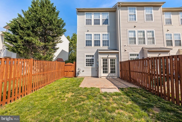 rear view of property featuring a lawn, a fenced backyard, a patio area, and a gate