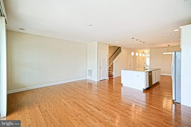 unfurnished living room with visible vents, baseboards, stairway, a sink, and light wood finished floors