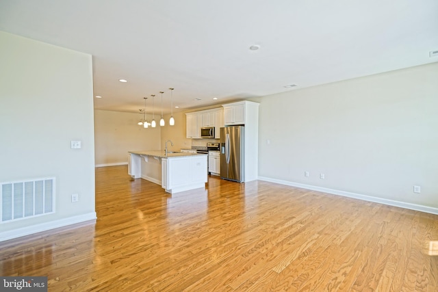 unfurnished living room with visible vents, light wood-type flooring, a sink, baseboards, and recessed lighting