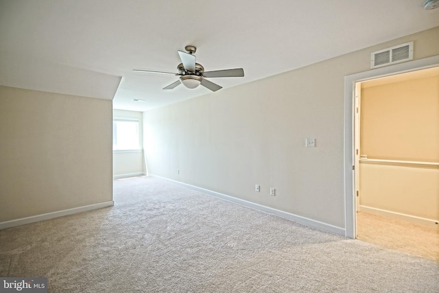 carpeted spare room with visible vents, baseboards, and ceiling fan