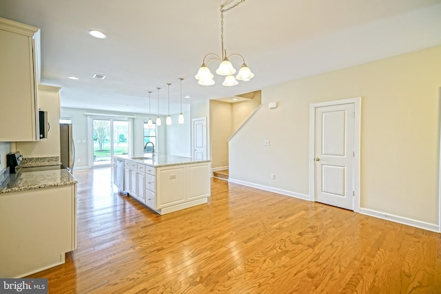 kitchen featuring appliances with stainless steel finishes, a sink, a chandelier, light wood-style flooring, and pendant lighting