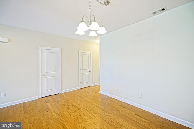 unfurnished dining area featuring baseboards, a notable chandelier, wood finished floors, and visible vents