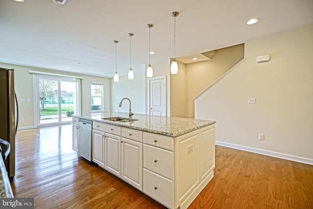 kitchen with appliances with stainless steel finishes, wood finished floors, a sink, light stone counters, and white cabinetry
