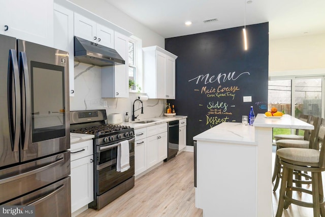 kitchen featuring a sink, a breakfast bar area, appliances with stainless steel finishes, under cabinet range hood, and visible vents
