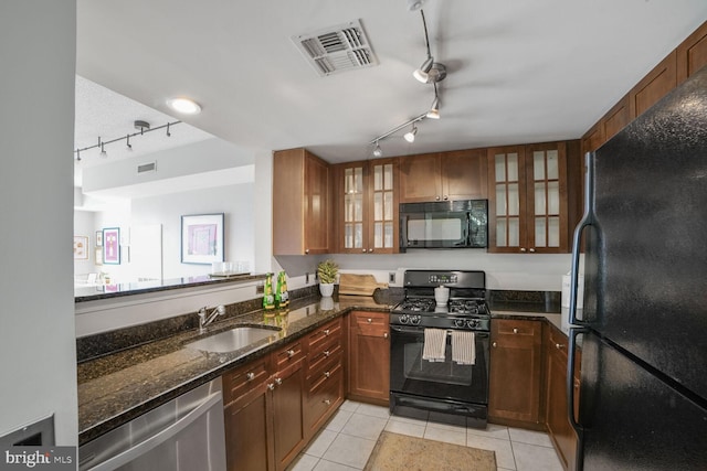 kitchen with track lighting, black appliances, a sink, light tile patterned floors, and dark stone counters