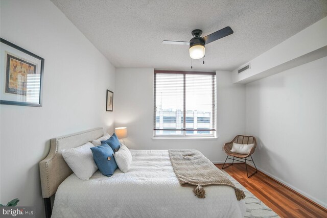 bedroom featuring wood finished floors, a textured ceiling, baseboards, and a ceiling fan