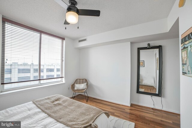 bedroom with wood finished floors, a textured ceiling, baseboards, and ceiling fan