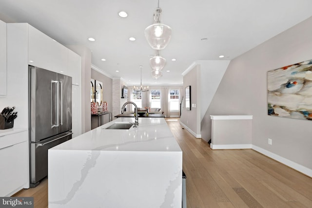 kitchen with a sink, ornamental molding, a kitchen island with sink, high end fridge, and white cabinetry