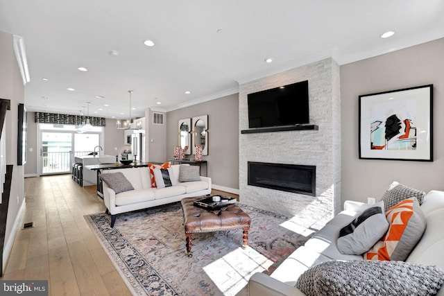 living room with a fireplace, light wood-style flooring, ornamental molding, recessed lighting, and a chandelier