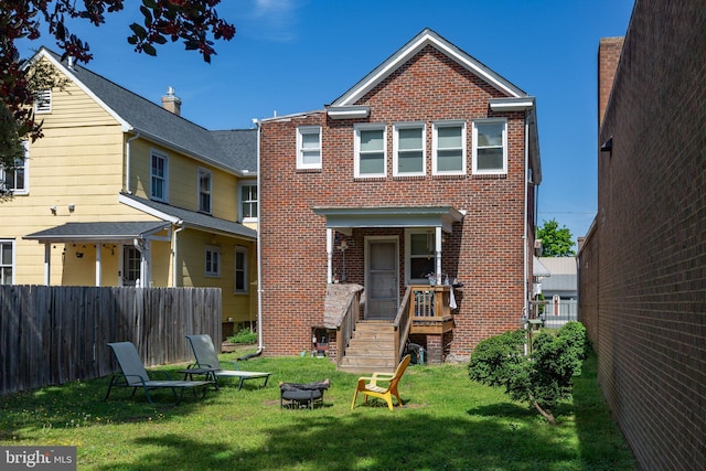 back of property with a lawn, fence, a fire pit, and brick siding