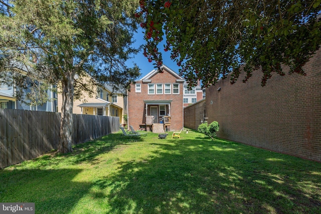 back of house featuring a lawn, fence, and brick siding