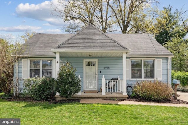 view of front facade featuring roof with shingles, a front yard, and covered porch