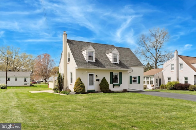 cape cod-style house featuring driveway, roof with shingles, a front yard, and stucco siding