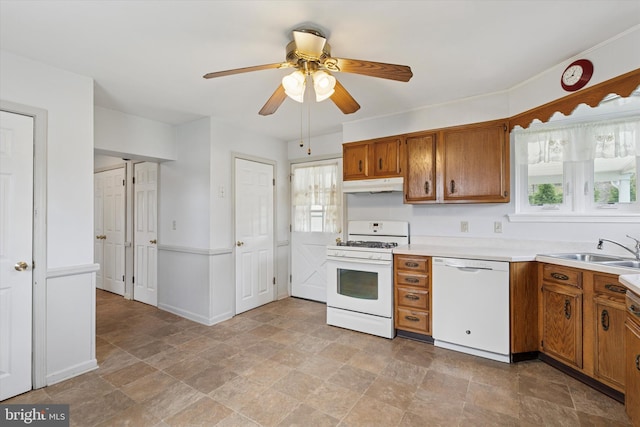 kitchen with brown cabinets, under cabinet range hood, a sink, and white appliances