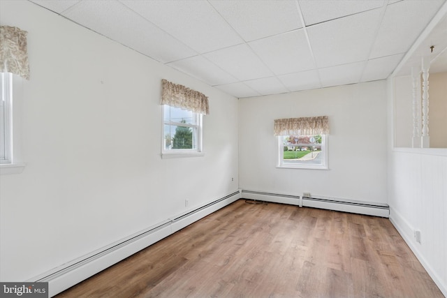 spare room with a paneled ceiling, baseboard heating, and wood finished floors