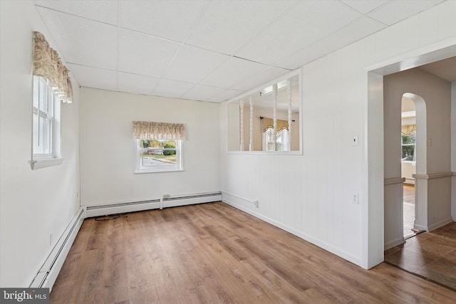 empty room with wood finished floors, a baseboard heating unit, arched walkways, baseboards, and a paneled ceiling