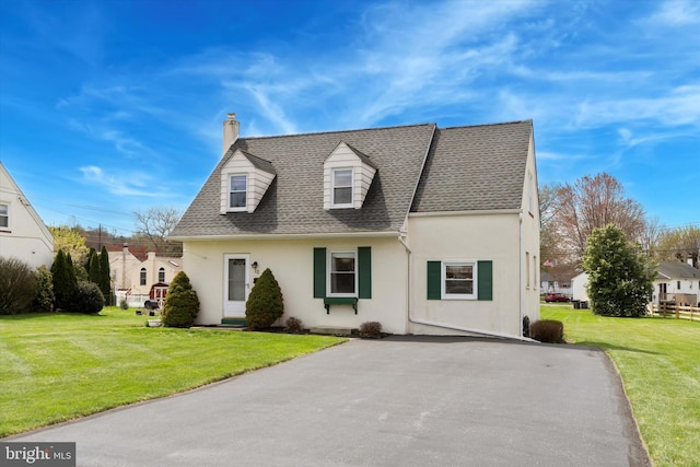 new england style home with a front lawn, a chimney, and stucco siding