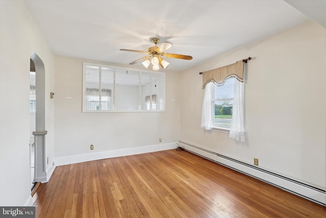 empty room with baseboard heating, hardwood / wood-style floors, ceiling fan, arched walkways, and baseboards