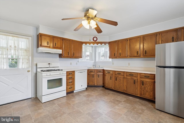 kitchen with a sink, white appliances, brown cabinets, light countertops, and under cabinet range hood