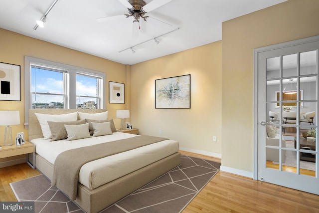 bedroom featuring rail lighting, baseboards, wood finished floors, and ceiling fan