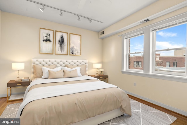 bedroom with track lighting, baseboards, wood finished floors, and visible vents