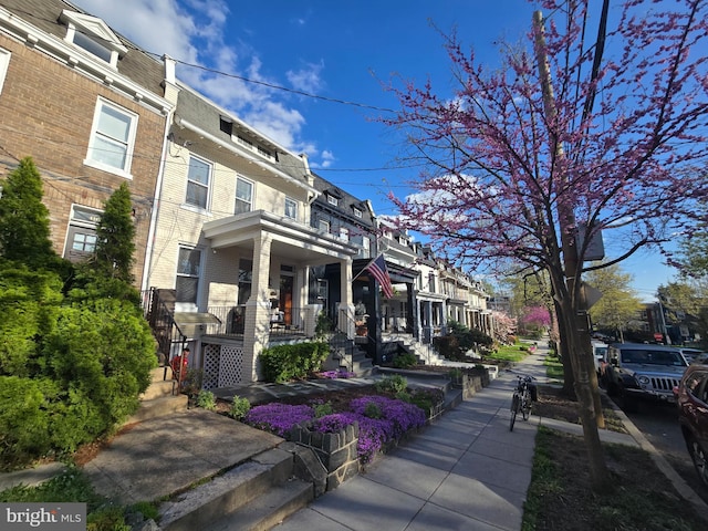 view of front of house featuring brick siding, mansard roof, a residential view, and covered porch