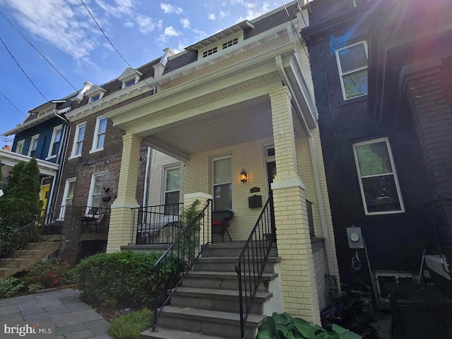 view of front of property with stairway, brick siding, and a porch