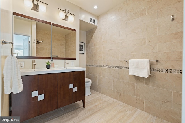 bathroom with tile walls, double vanity, and toilet