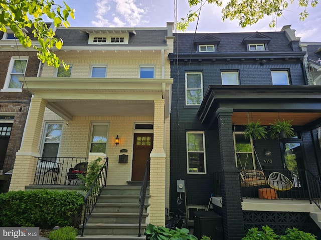 multi unit property with mansard roof, covered porch, and brick siding