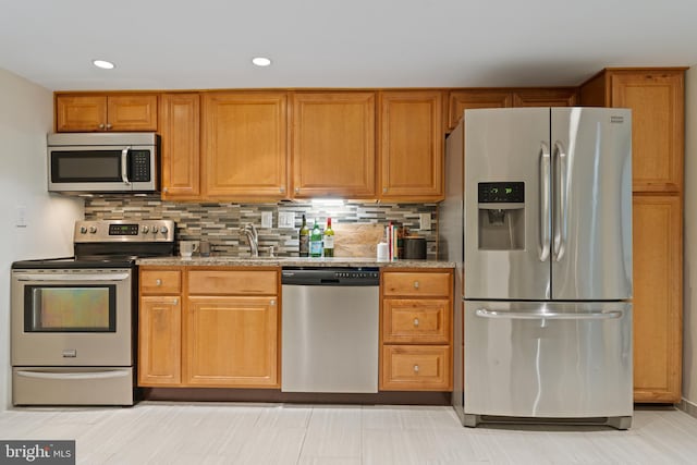 kitchen featuring stainless steel appliances, a sink, tasteful backsplash, recessed lighting, and brown cabinetry