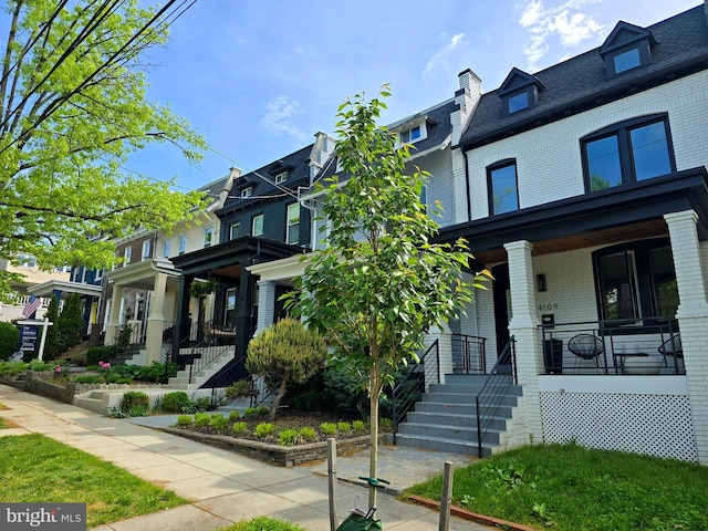 view of front of house with brick siding, covered porch, mansard roof, and stairs