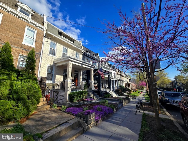 view of property featuring mansard roof, brick siding, a residential view, and covered porch