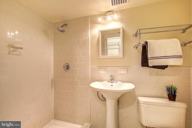 full bath with wainscoting, toilet, tile walls, visible vents, and tiled shower